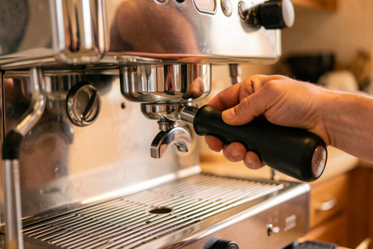Home barista locking a blind portafilter into a chrome espresso group head to backflush