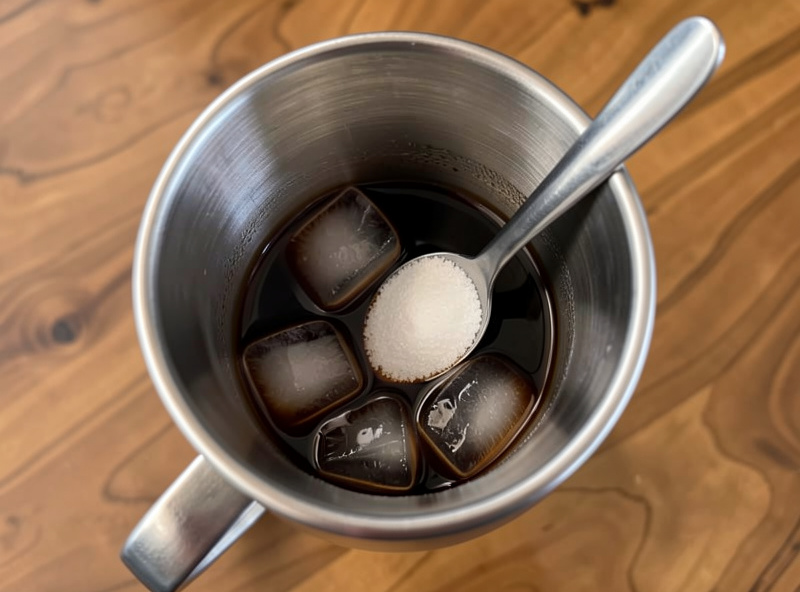 Espresso, ice, and sugar being shaken hard in a stainless cocktail shaker