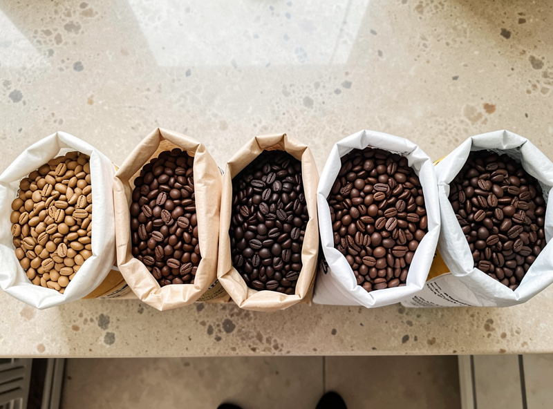 Several open bags of espresso beans of different roast levels lined up on a kitchen counter for comparison