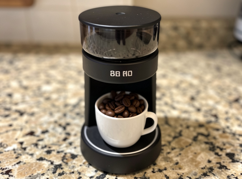 A single-dose espresso grinder with a small bean cup holding one shot of weighed coffee beans on a counter