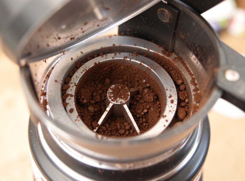 Coffee grounds clinging inside the chute and burr chamber of an opened espresso grinder, illustrating retention