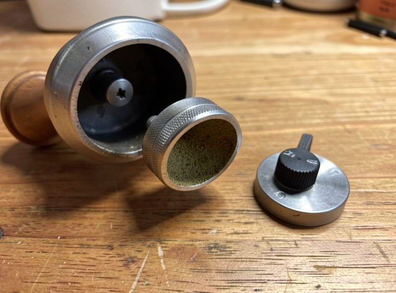 A hand grinder disassembled showing its conical burr and adjustment dial on a wooden surface