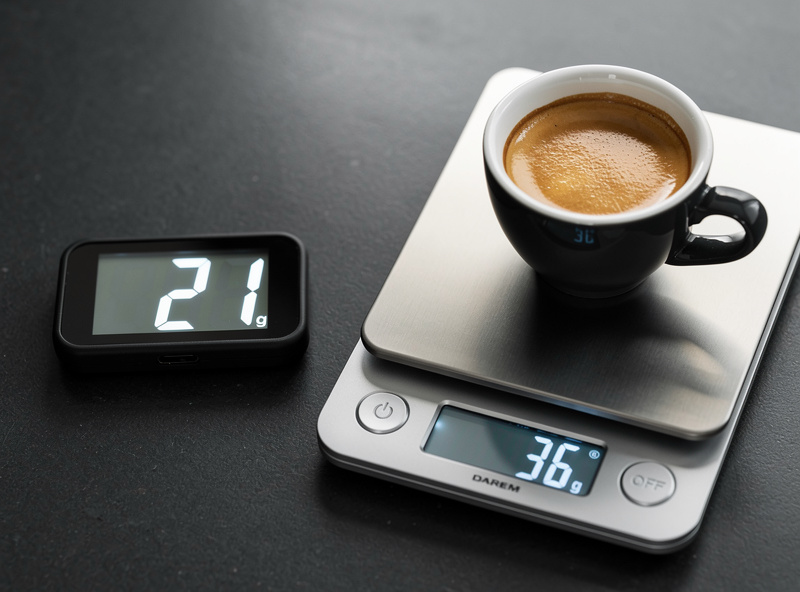 An espresso shot timer reading 27 seconds beside a scale showing 36 grams of espresso, a balanced shot result