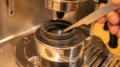 Worn espresso group gasket being eased out of a chrome E61 group head with a pick tool