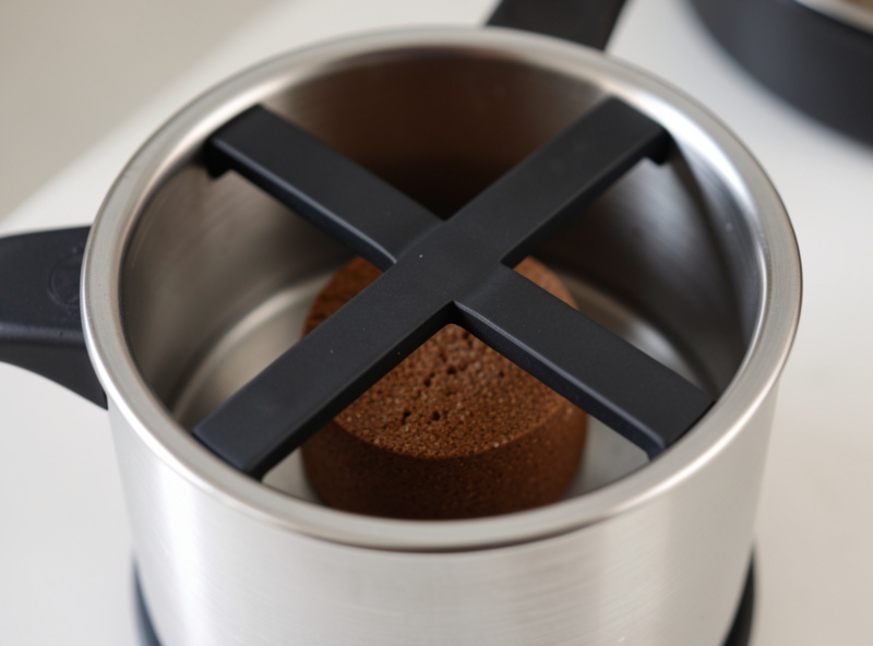 A stainless steel espresso knock box with a rubber crossbar holding spent coffee pucks